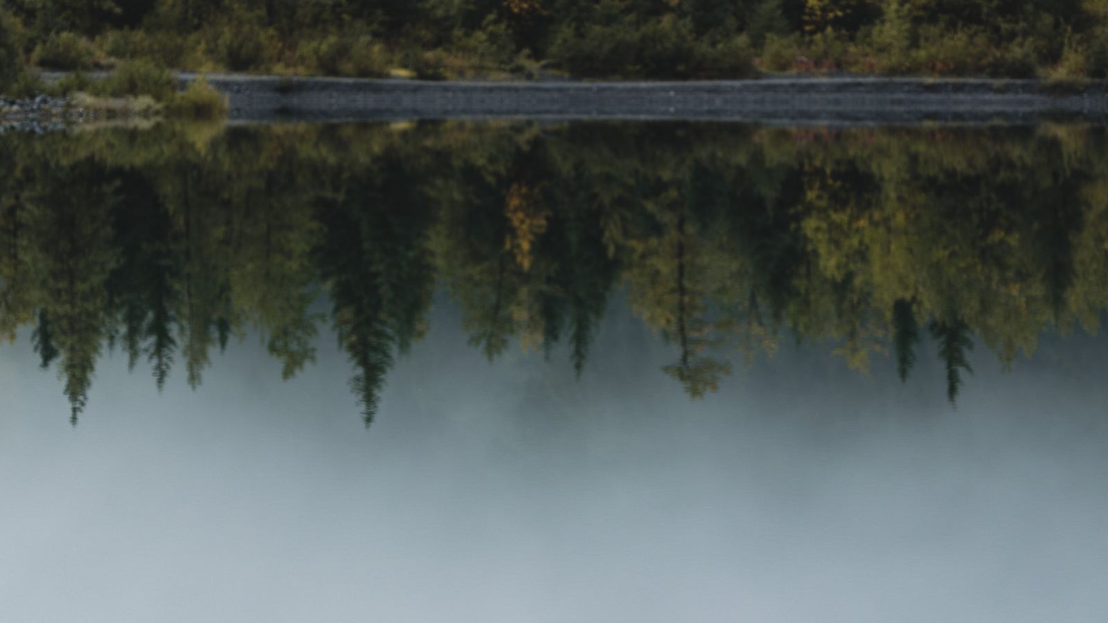 A glassy lake at golden hour mirroring an autumn treeline, the surface completely still.