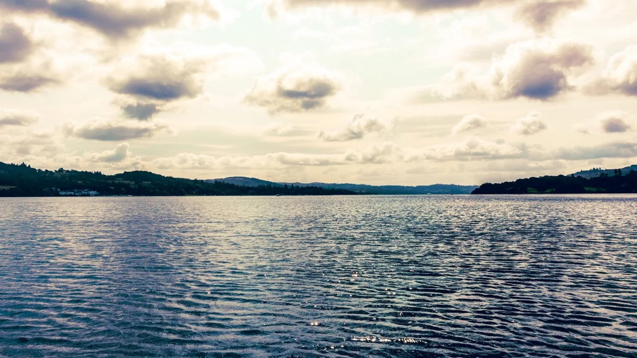 A broad lake below rolling hills under a moody sky, an inviting stretch of open water to explore.