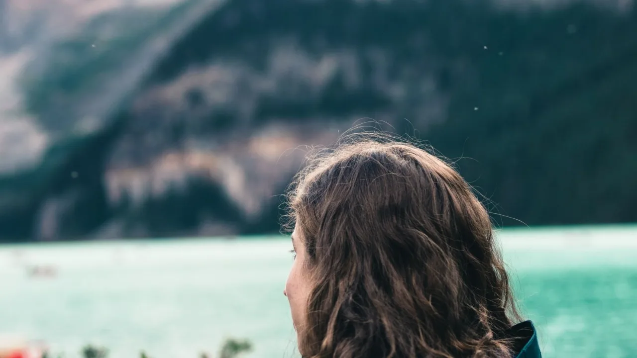 A person looking out over calm water toward distant hills, weighing the day.