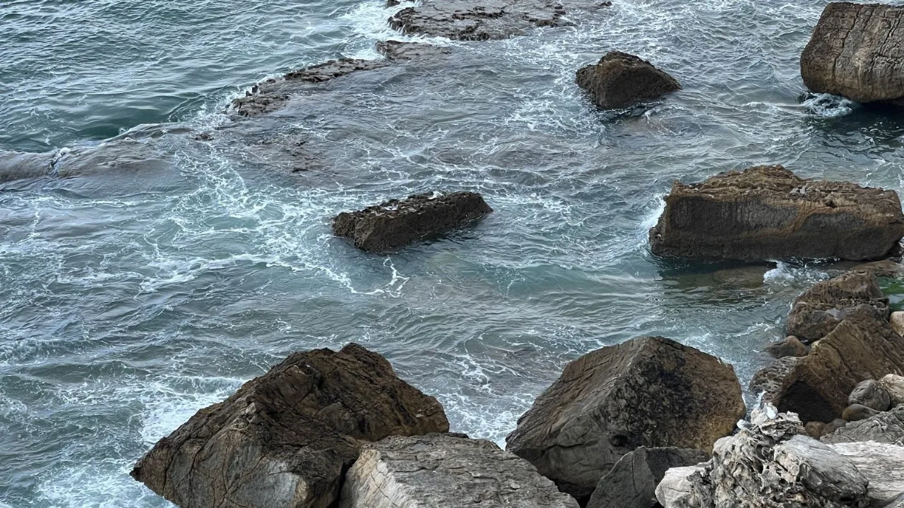 Waves breaking white around dark rocks along a rugged, exposed stretch of coast.