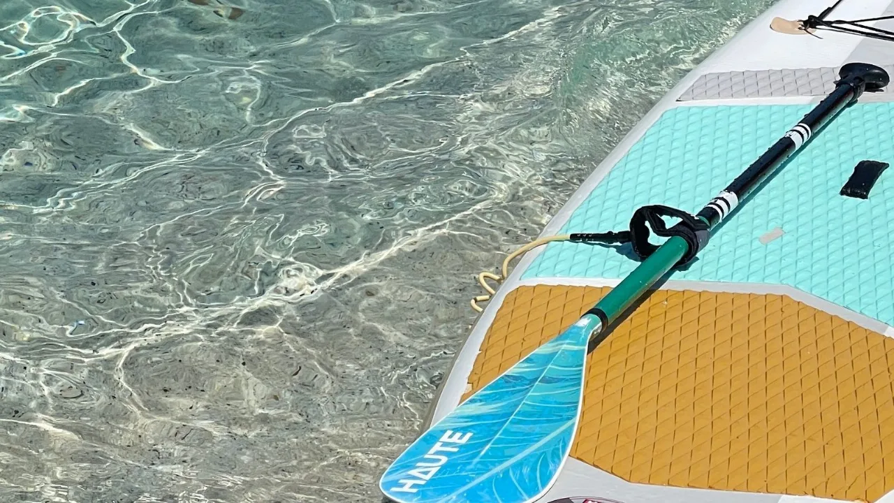 A paddleboard and paddle resting on clear, shallow water at the edge of a launch.